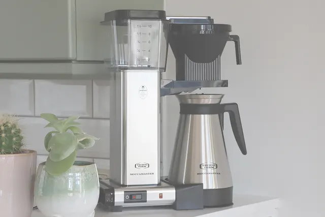 Moccamaster KBGT Silver virtuvėje prie plytelėmis išklotos sienos
